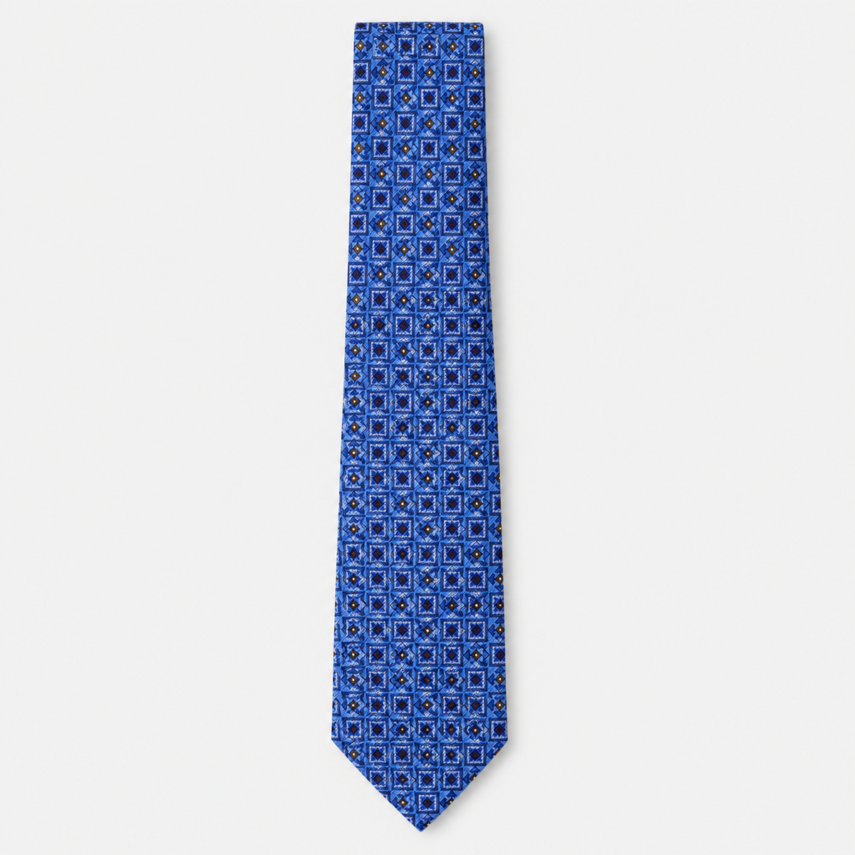 The Catania Tie, a blue silk tie with navy, light blue and gold square motifs on a light grey background.