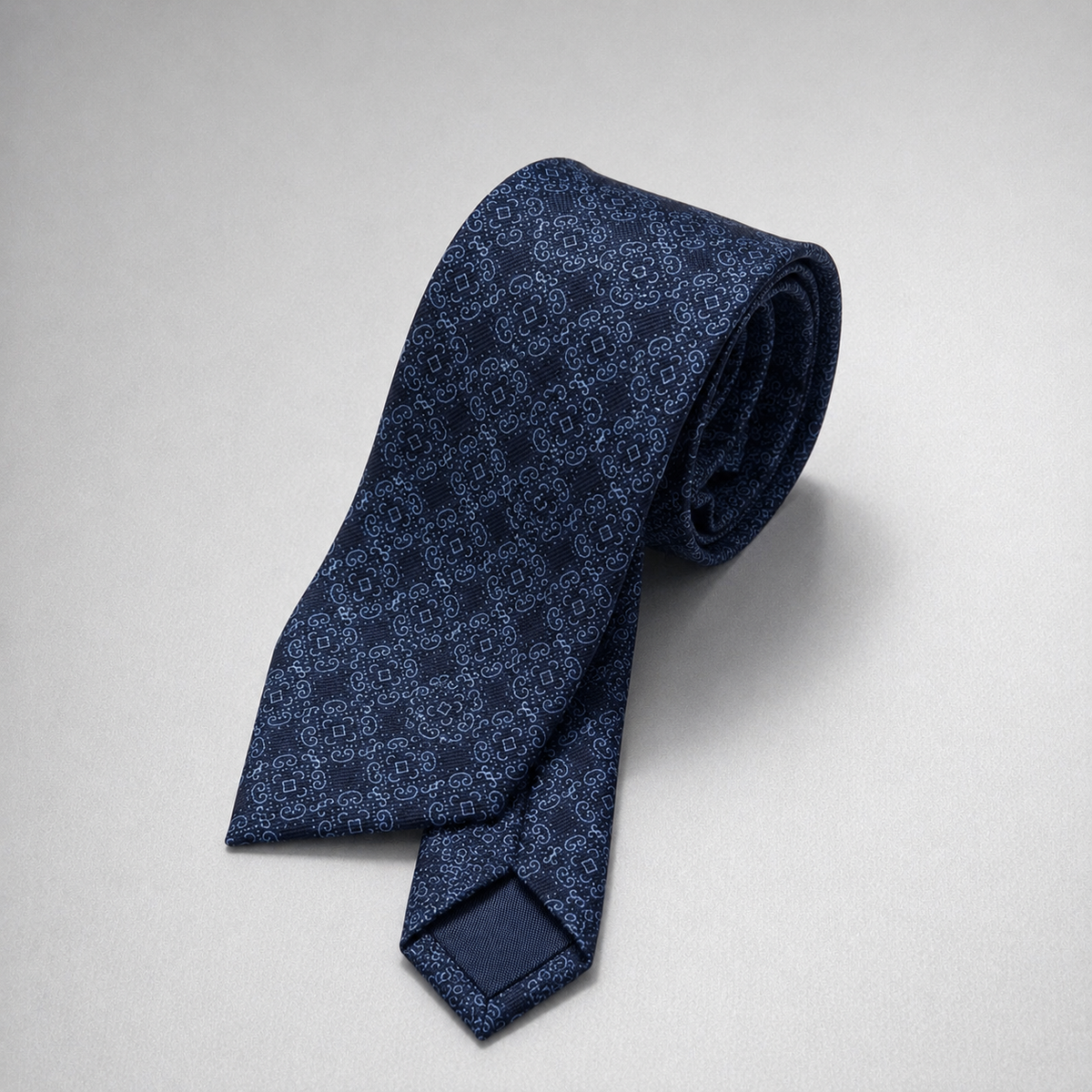 Navy tonal floral silk necktie on a grey background.