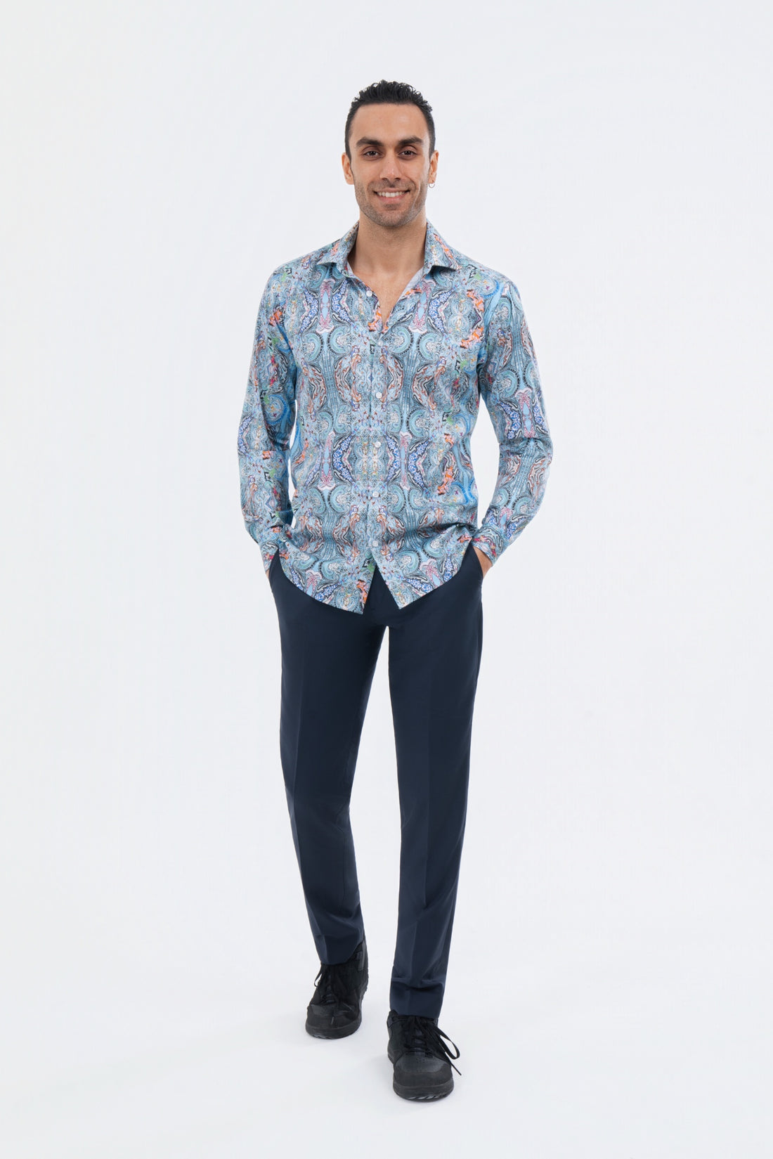 Male model wearing a turquoise paisley shirt with navy trousers in the studio.