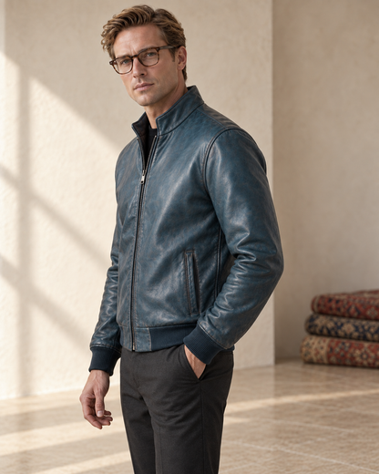 Male model wearing the Teal Patina Lambskin Leather Bomber beside a minimal stack of rugs