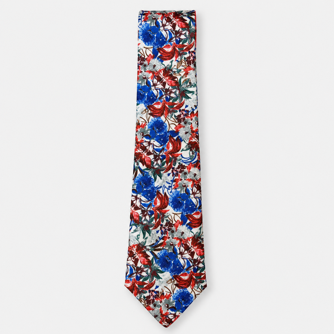 The Assisi Tie, an ivory silk tie with a vivid red, blue and green botanical print on a light grey background.