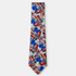 The Assisi Tie, an ivory silk tie with a vivid red, blue and green botanical print on a light grey background.