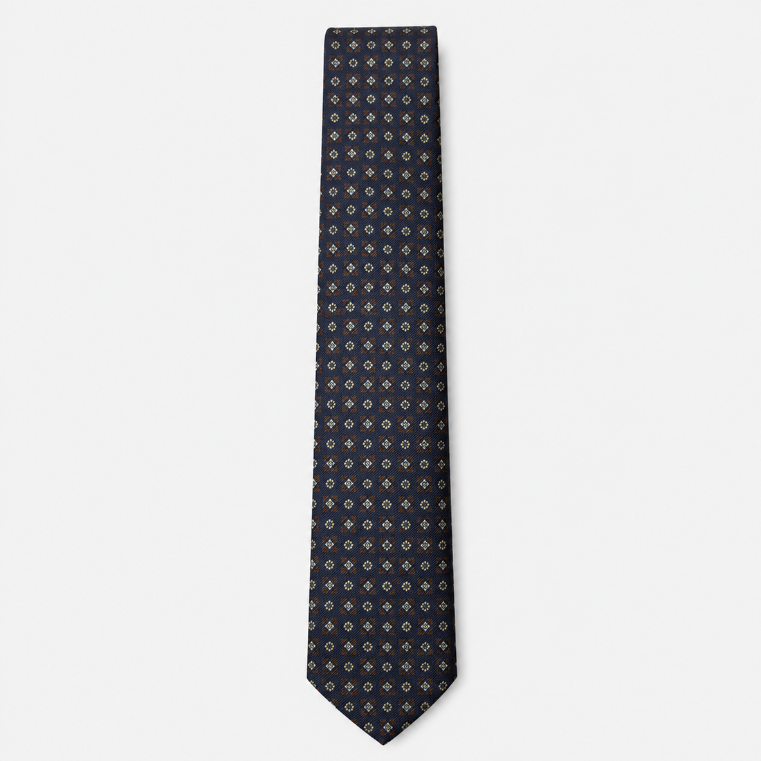 The Bolzano Tie – navy, gold and rust micro medallion silk tie on a light grey background