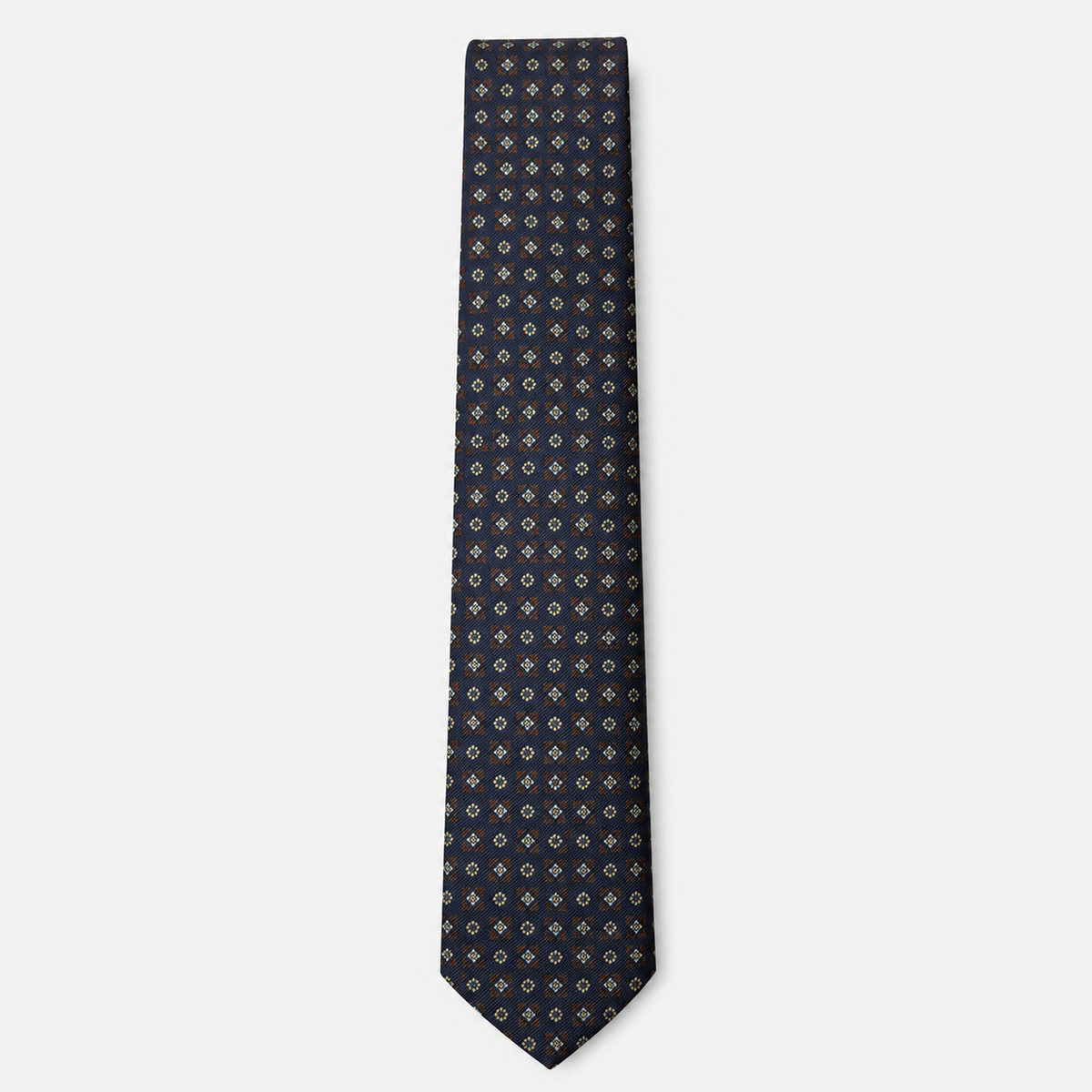 The Bolzano Tie – navy, gold and rust micro medallion silk tie on a light grey background