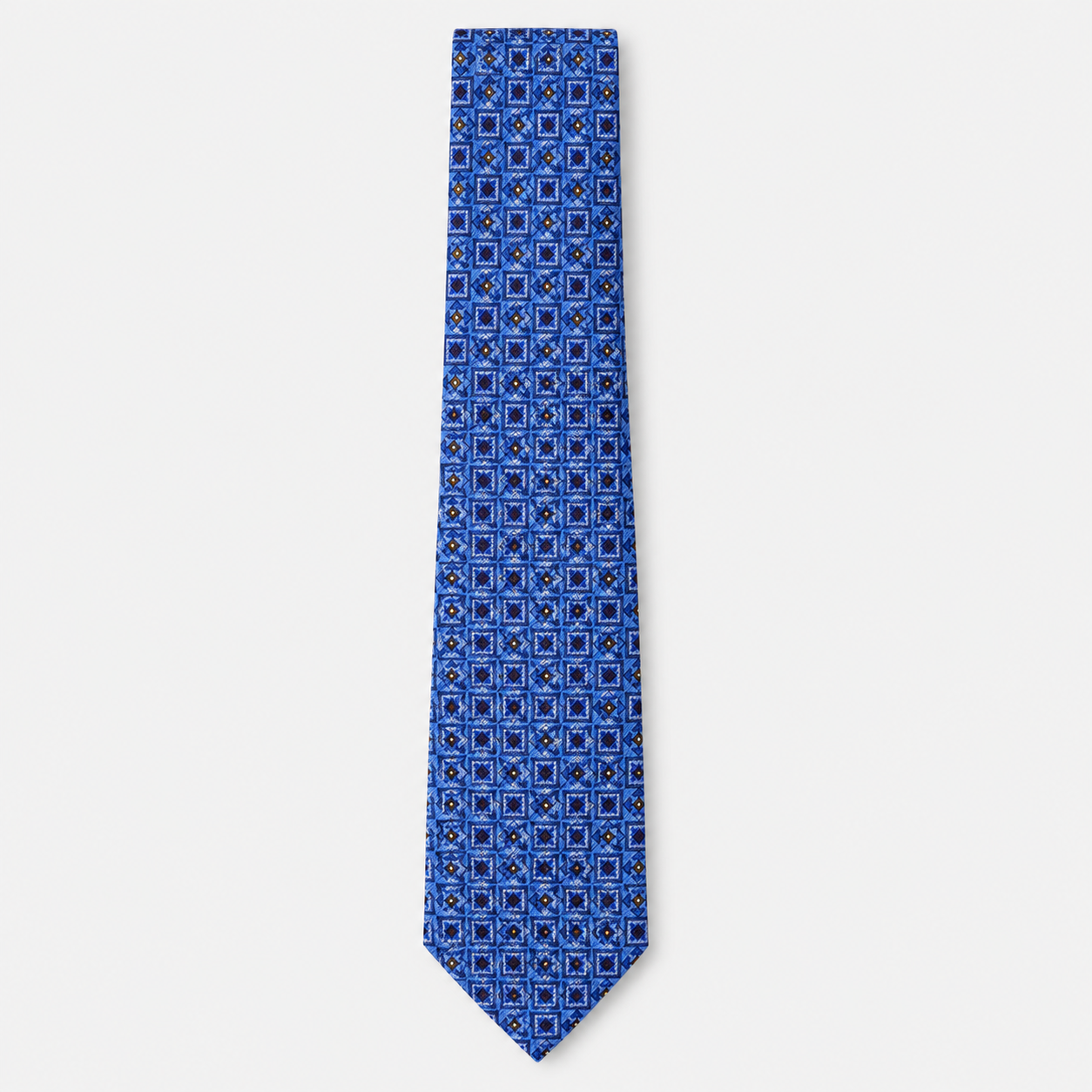 The Catania Tie, a blue silk tie with navy, light blue and gold square motifs on a light grey background.