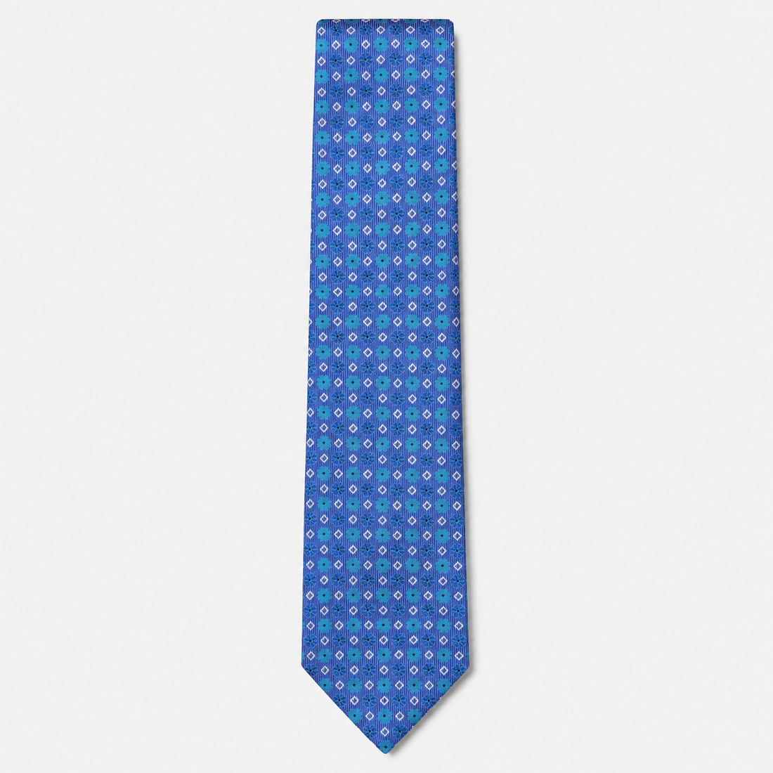 The Ferrara Tie, a royal blue silk tie with turquoise, lavender and white geometric motifs on a light grey background.