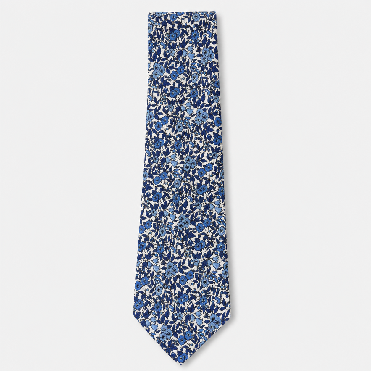 The Genova Tie, an ivory silk tie with a dense navy and blue floral print on a light grey background.