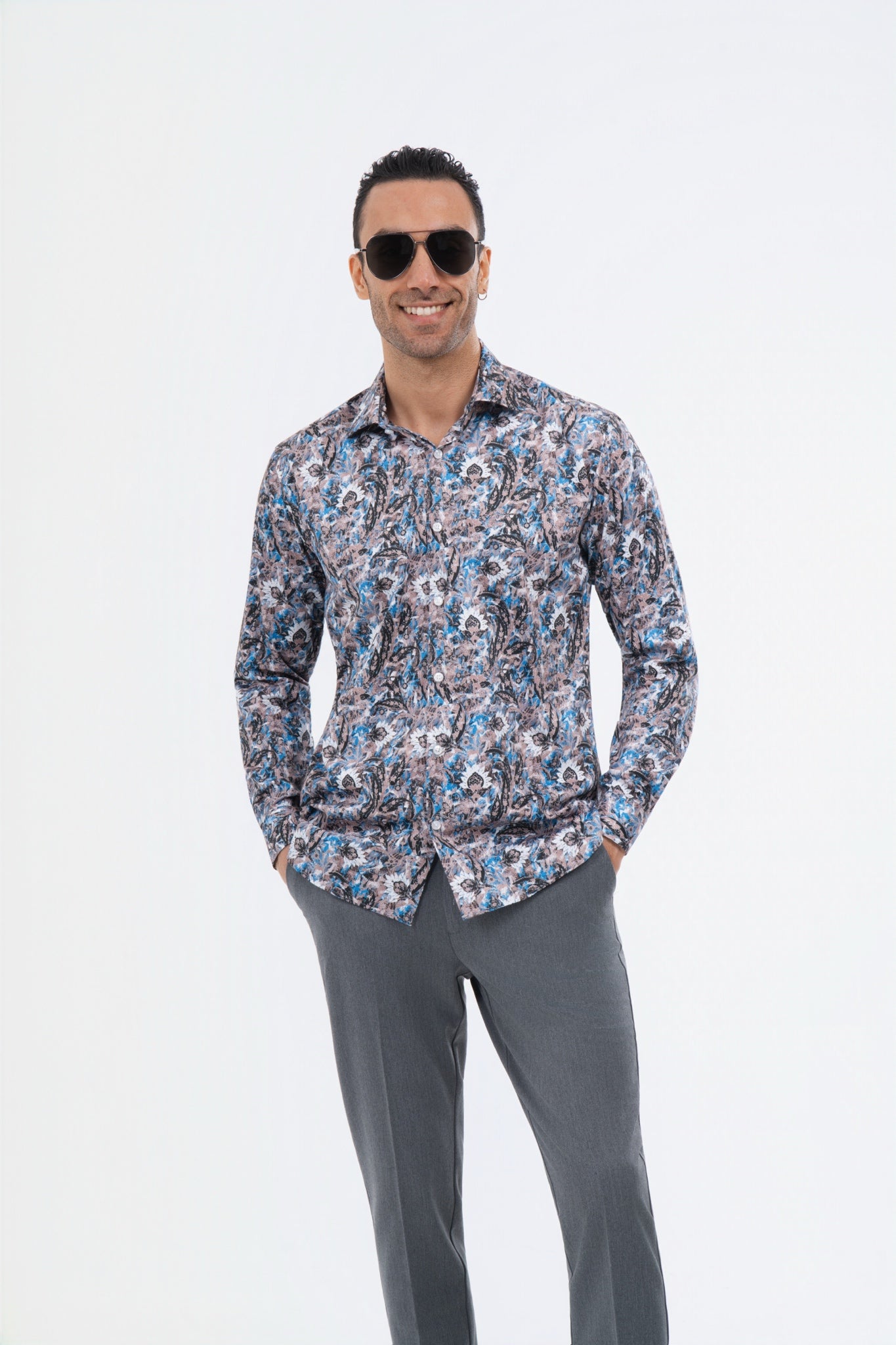 Male model wearing a multicolour paisley shirt with grey trousers in the studio.