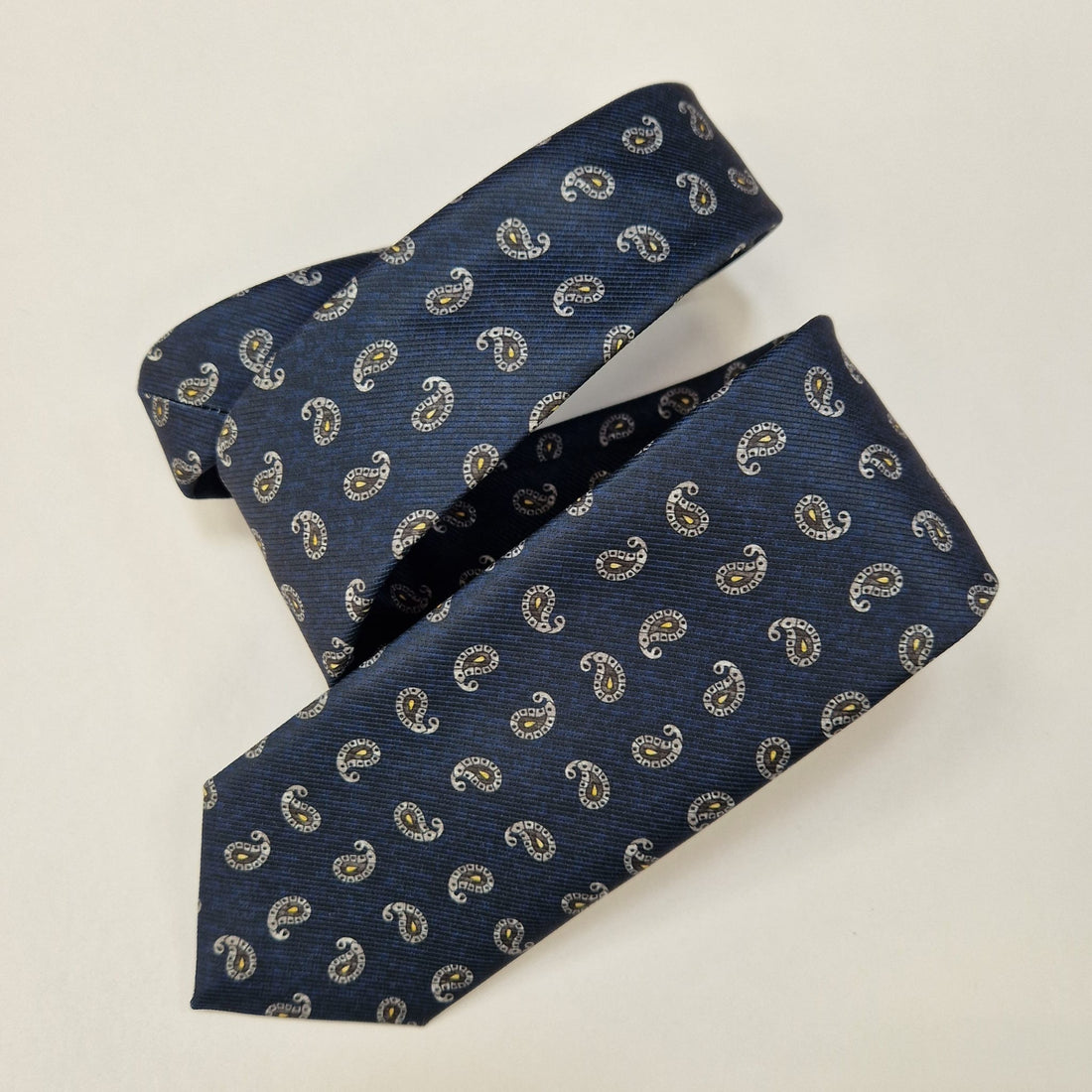 Navy silk tie with small silver paisley motifs, loosely folded.