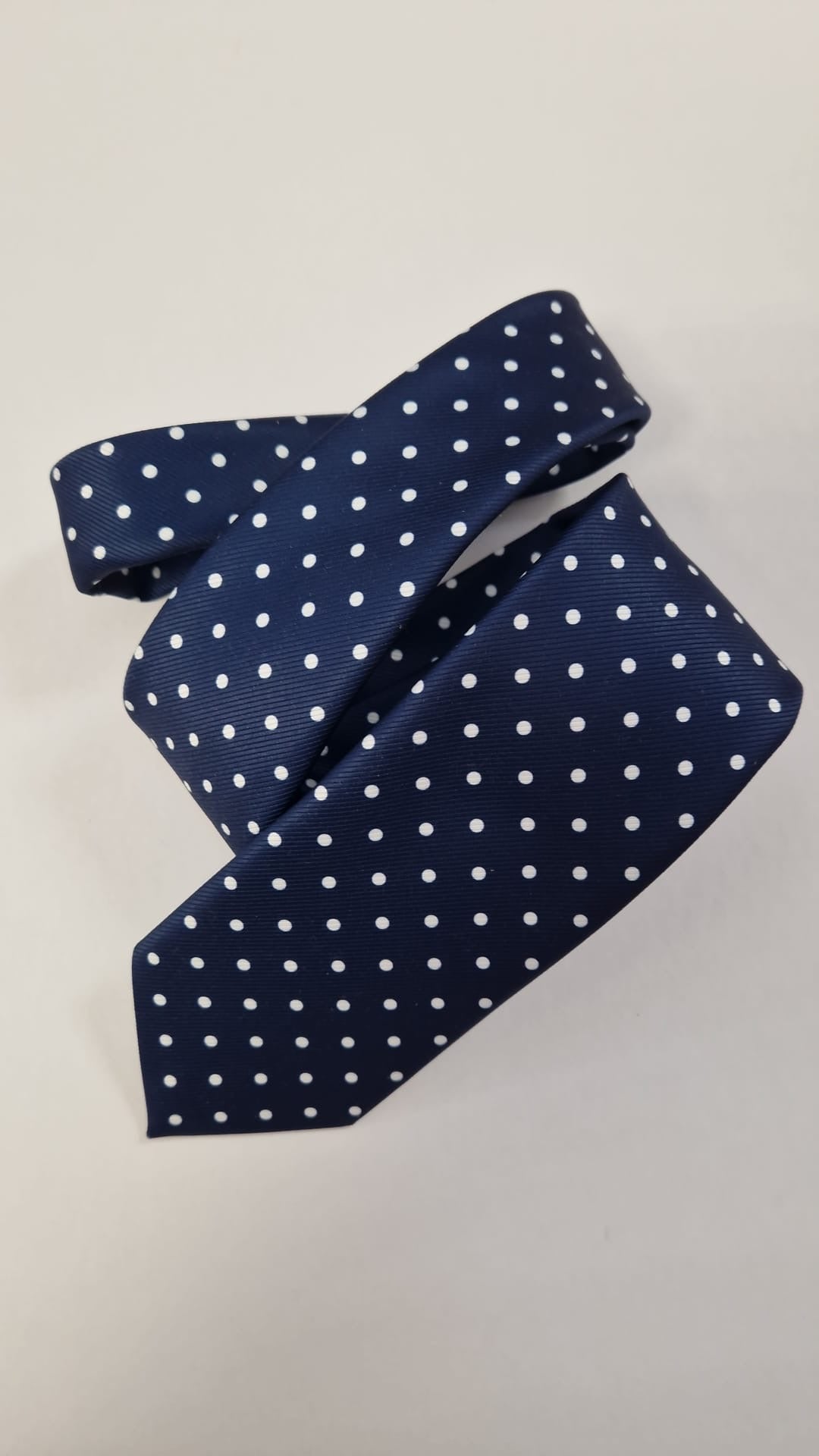 Navy silk tie with white polka dots, loosely folded.
