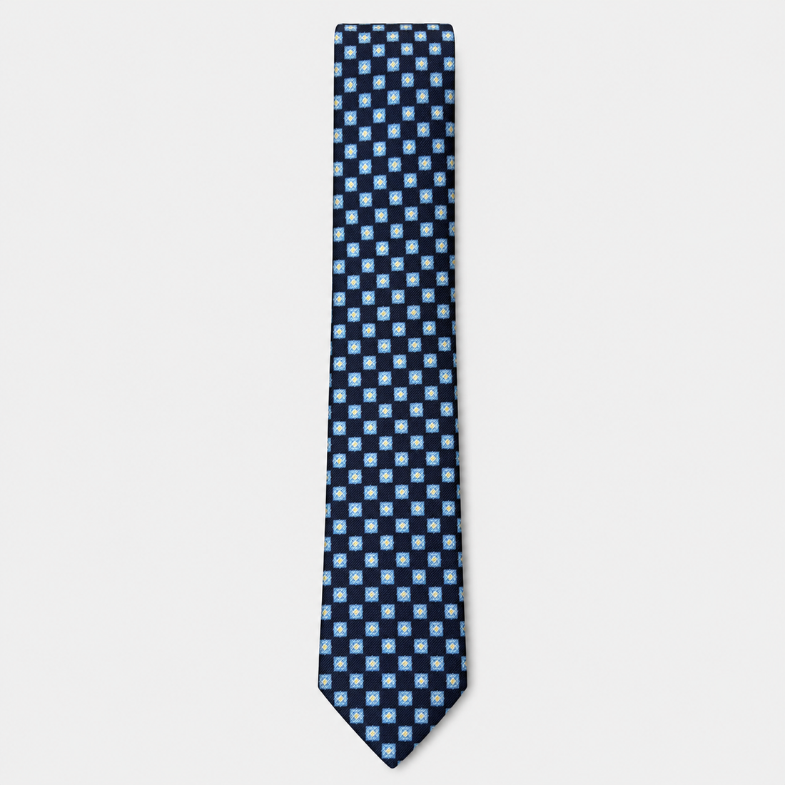 The Novara Tie – navy and white checkerboard silk tie on a light grey background
