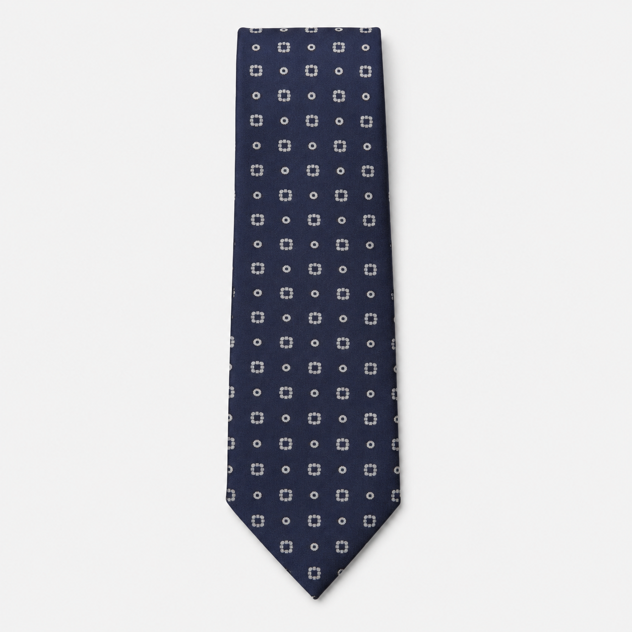 The Orvieto Tie, a navy silk tie with small white geometric dot motifs on a light grey background.