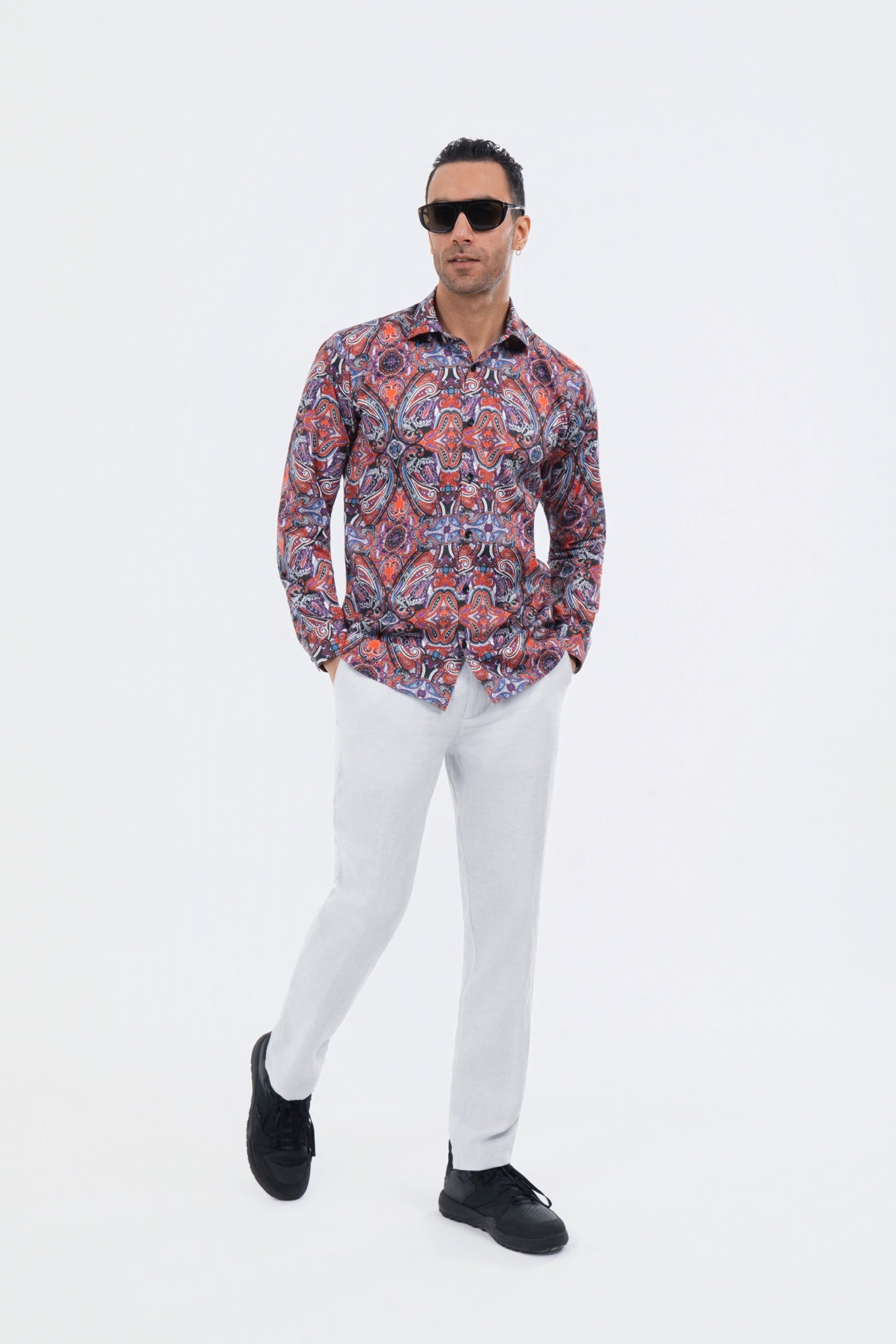 Male model wearing a red and navy paisley shirt with white trousers.