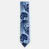 The Taormina Tie, an ivory silk tie with navy tropical leaves and light blue diagonal stripes on a light grey background.